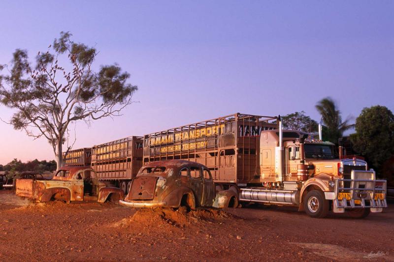 Three-trailer road train travelling passt old cars at the roadside