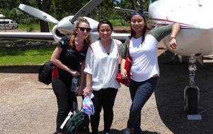 Three young women standing beside a small plane